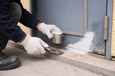 奈良市ハイツケレン後の玄関ドア下部にサビ止め塗料を塗布し、腐食の進行を防いでいる施工工程