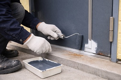 奈良市ハイツ玄関ドア塗装工事の上塗り作業中の様子　耐久性と美観を高めるためローラーで仕上げ